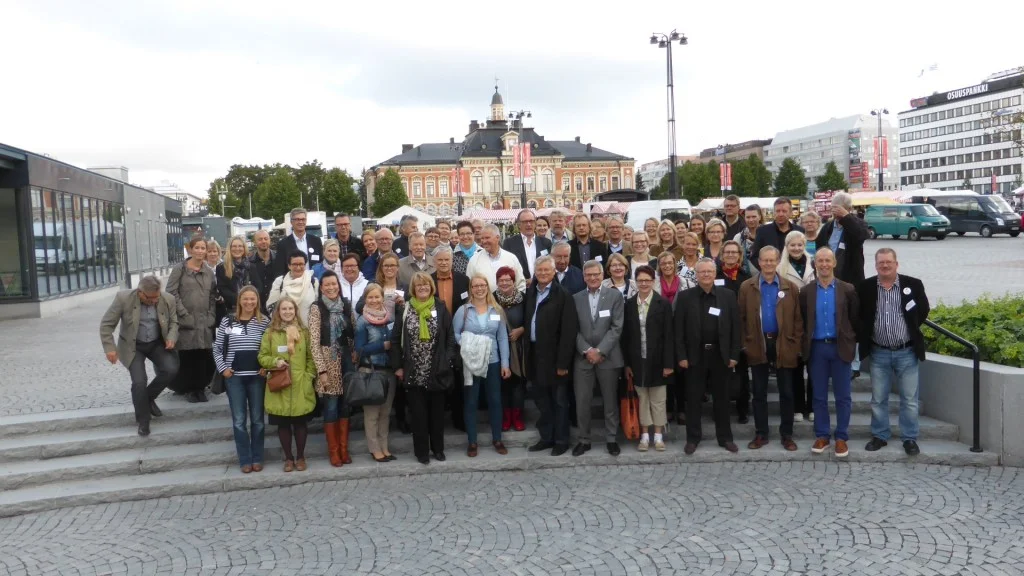 Konferenssin osanottajia Kuopion torilla. Taustalla tapahtumapaikka, Kuopion kaupungintalo